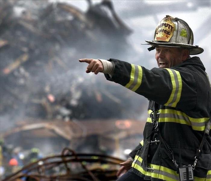 A firefighter stands in front of a burnt building