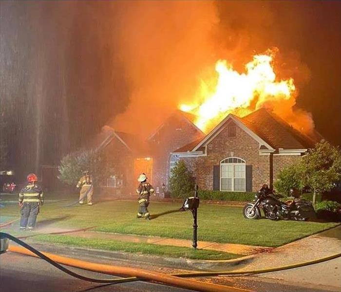 Firefighters on a lawn in front of a burning house